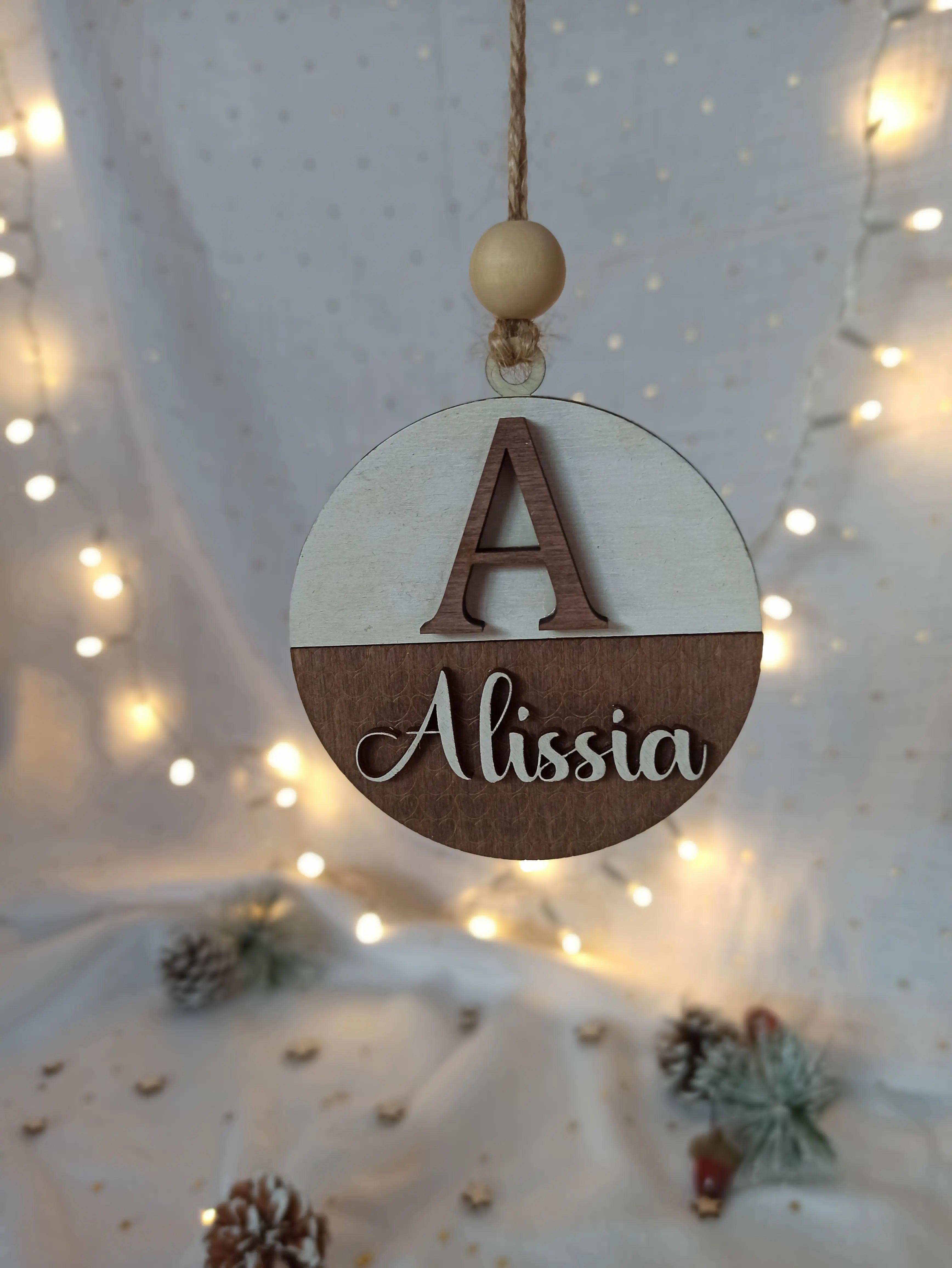Détail de la suspension “Prénom” en bois gravé, avec lettres superposées et perle en bois sur cordelette naturelle, décoration de Noël personnalisée