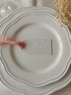 Marque-place en plexiglas personnalisé avec ruban en mousseline rose sur assiette de mariage